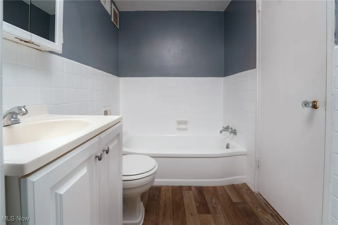 Full bath with visible vents, toilet, a bathing tub, wood finished floors, and vanity