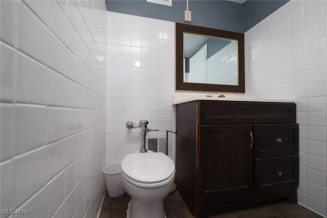 Bathroom featuring vanity, tile walls, and toilet
