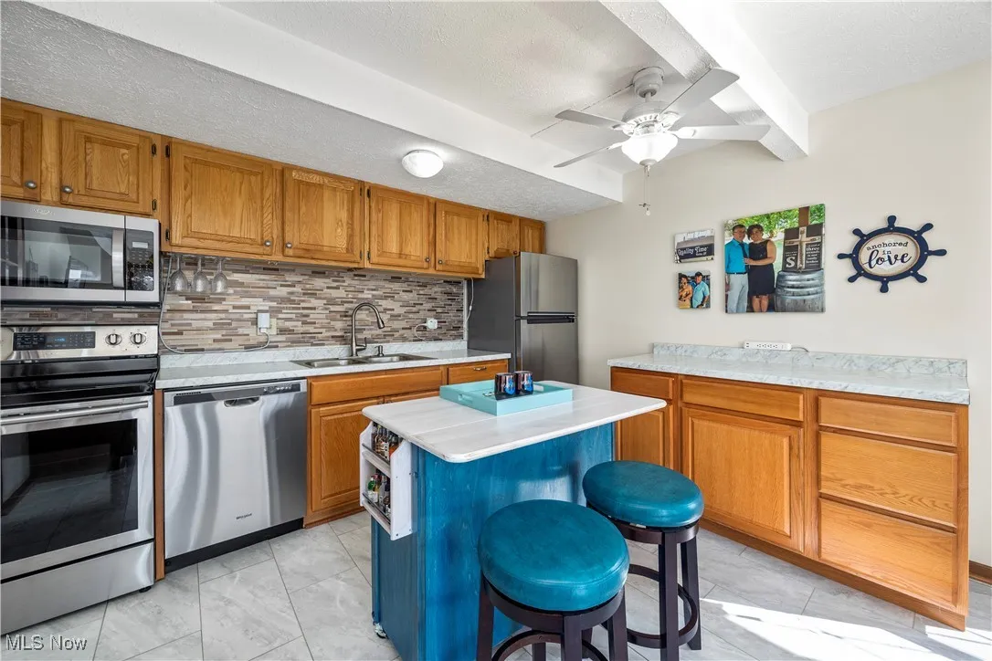 Kitchen featuring light countertops, decorative backsplash, brown cabinets, appliances with stainless steel finishes, and a sink
