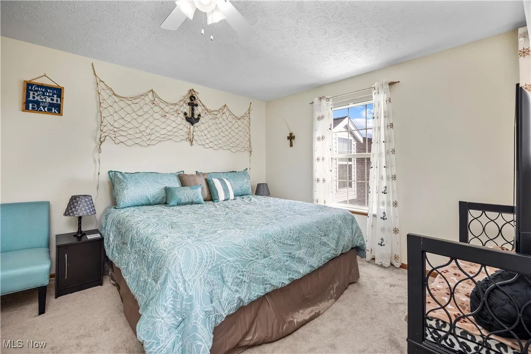 Bedroom featuring ceiling fan, light colored carpet, and a textured ceiling