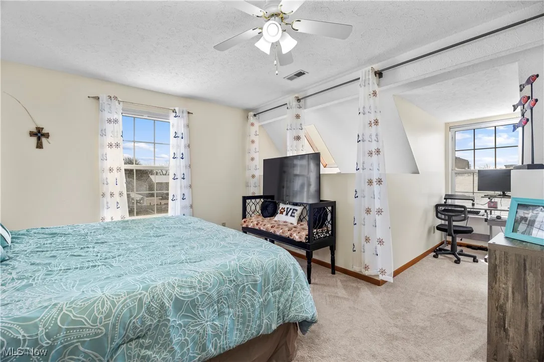 Bedroom with visible vents, multiple windows, a textured ceiling, and carpet flooring
