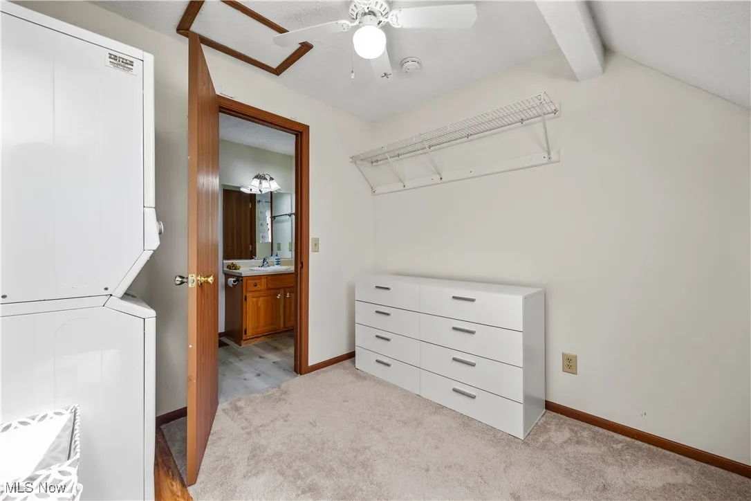 Spacious closet with a sink, light carpet, ceiling fan, and stacked washing maching and dryer