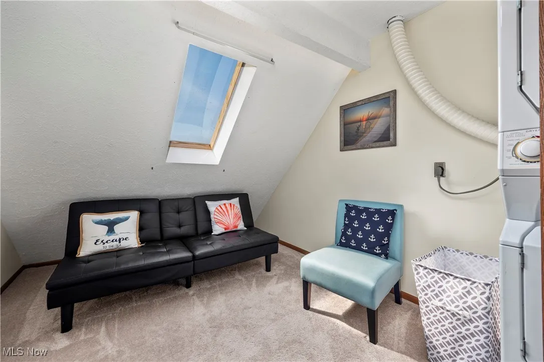 Living area with lofted ceiling with skylight, carpet, and baseboards