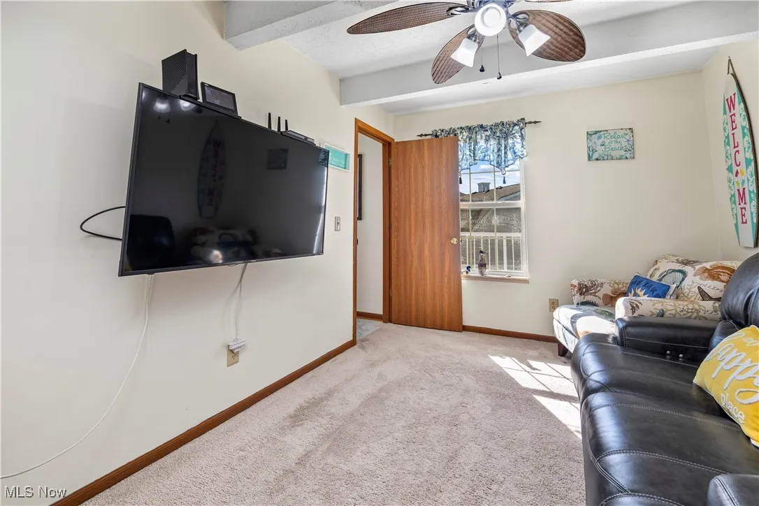 Carpeted living room with beamed ceiling, baseboards, and a ceiling fan