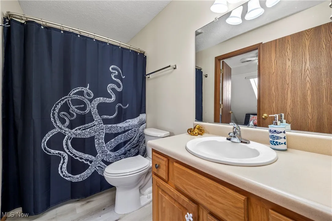Full bath with vanity, a shower with curtain, wood finished floors, a textured ceiling, and toilet