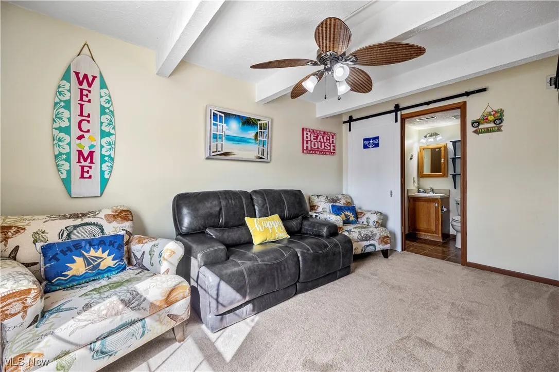 Carpeted living room with baseboards, a barn door, beam ceiling, a textured ceiling, and a ceiling fan