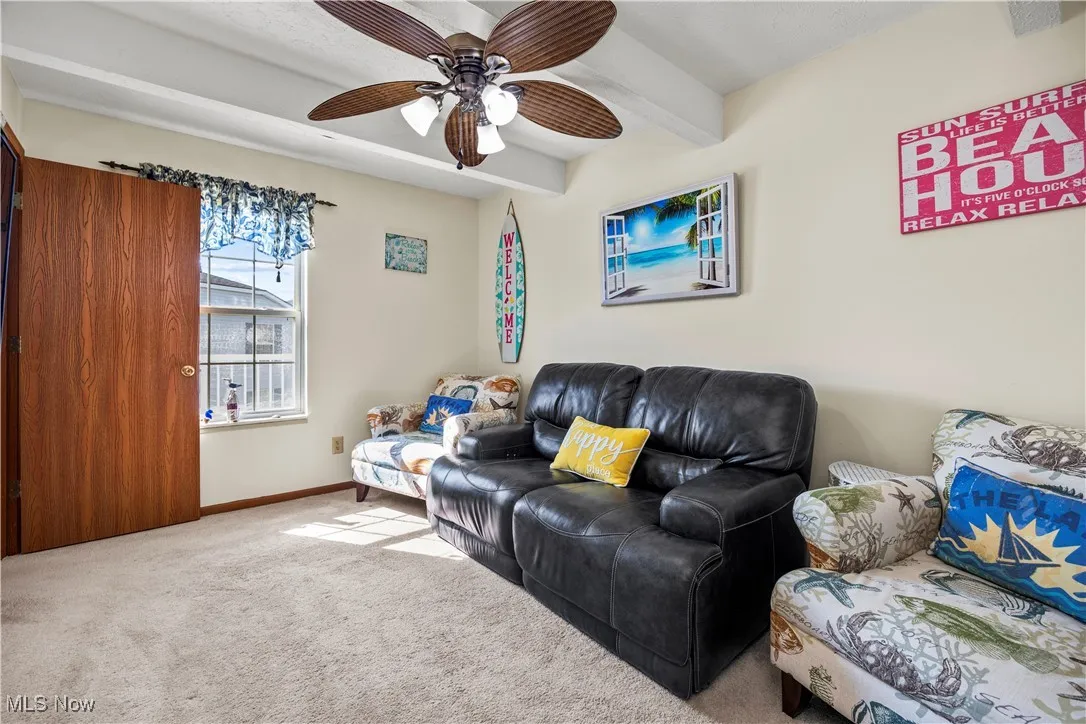 Living area with beam ceiling, carpet flooring, ceiling fan, and baseboards