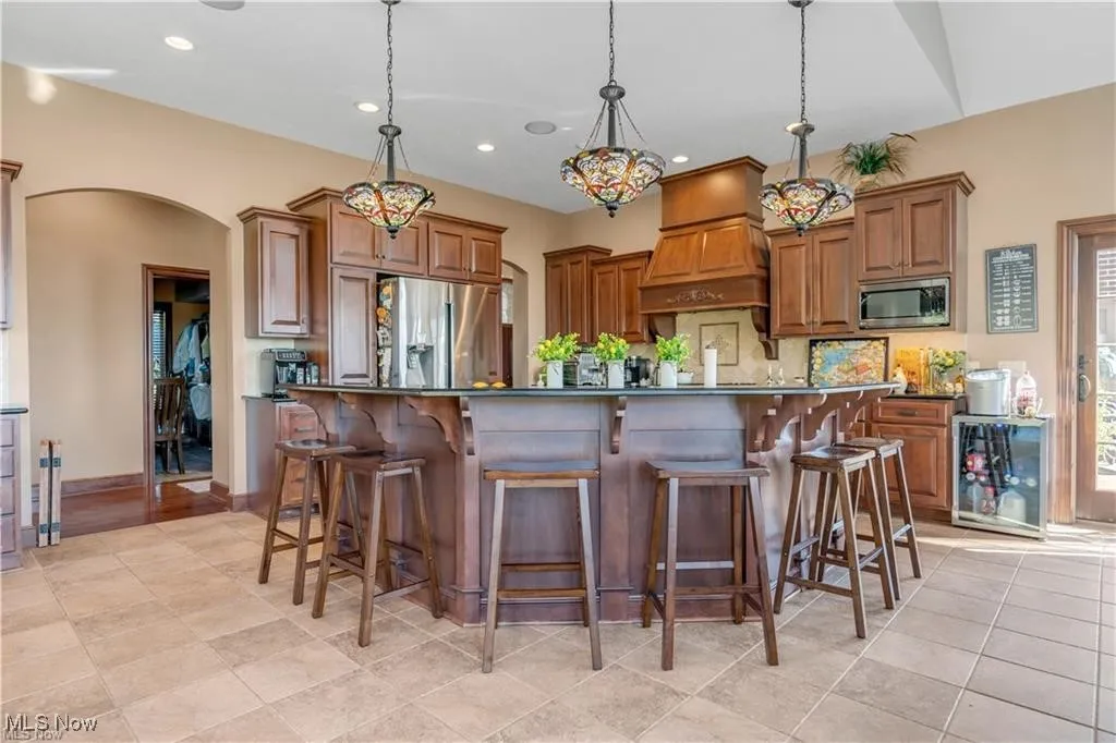Kitchen featuring dark countertops, appliances with stainless steel finishes, premium range hood, and arched walkways