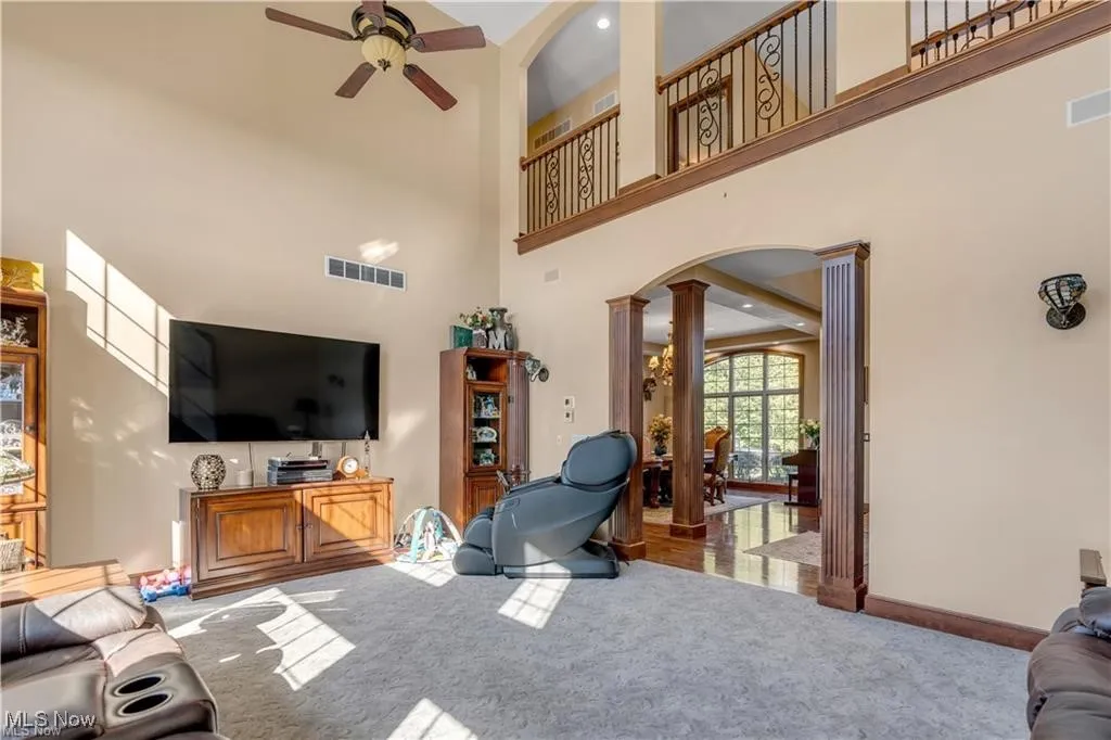 Carpeted living room with visible vents, a ceiling fan, arched walkways, a high ceiling, and ornate columns