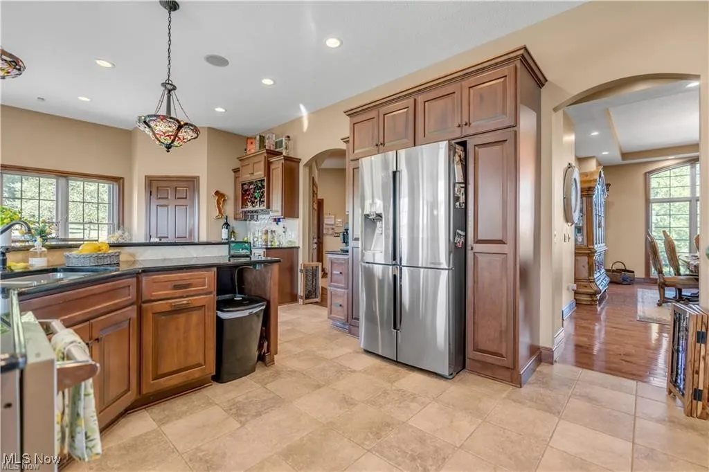 Kitchen featuring brown cabinetry, recessed lighting, arched walkways, a sink, and stainless steel refrigerator with ice dispenser