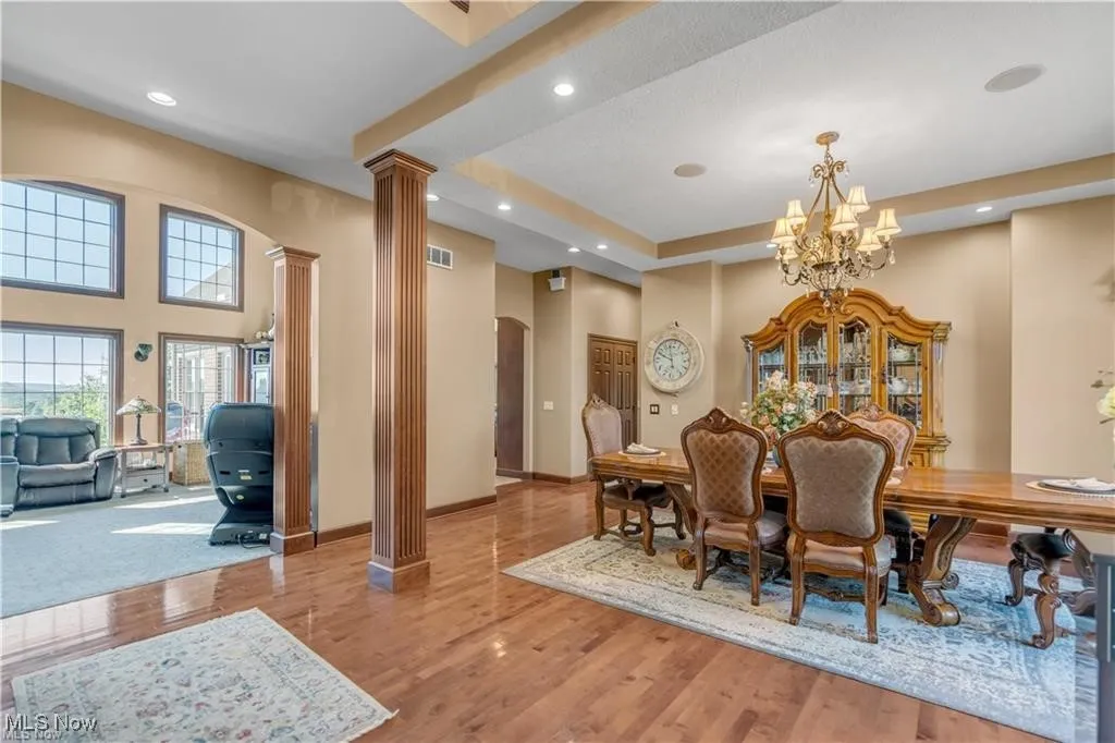 Dining area with wood finished floors, baseboards, ornate columns, an inviting chandelier, and arched walkways