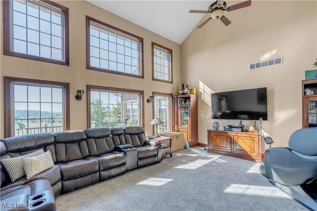 Carpeted living room featuring visible vents, high vaulted ceiling, and ceiling fan