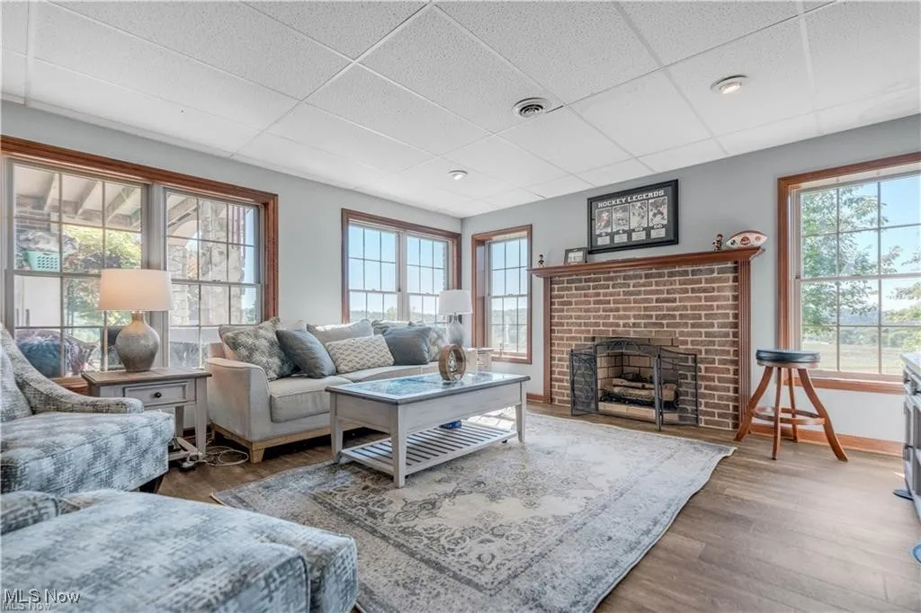 Living area featuring visible vents, a brick fireplace, baseboards, a drop ceiling, and wood finished floors