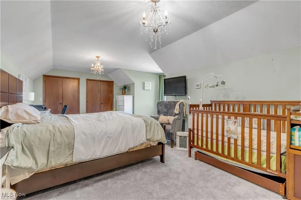 Bedroom with two closets, carpet floors, a notable chandelier, and lofted ceiling