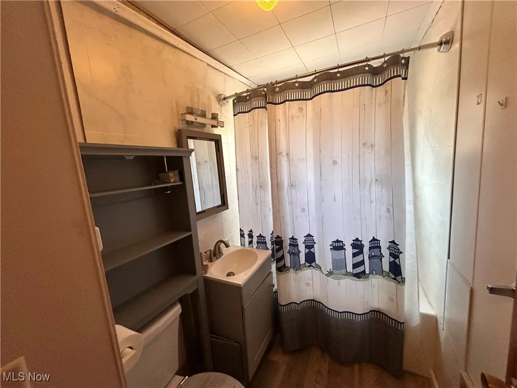 Full bath featuring vanity, wooden walls, wood finished floors, shower / bath combo, and toilet