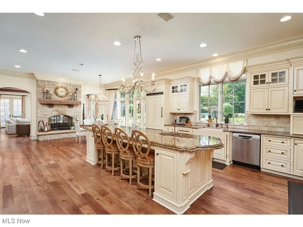 Kitchen featuring a chandelier, dishwasher, ornamental molding, a stone fireplace, and a kitchen breakfast bar