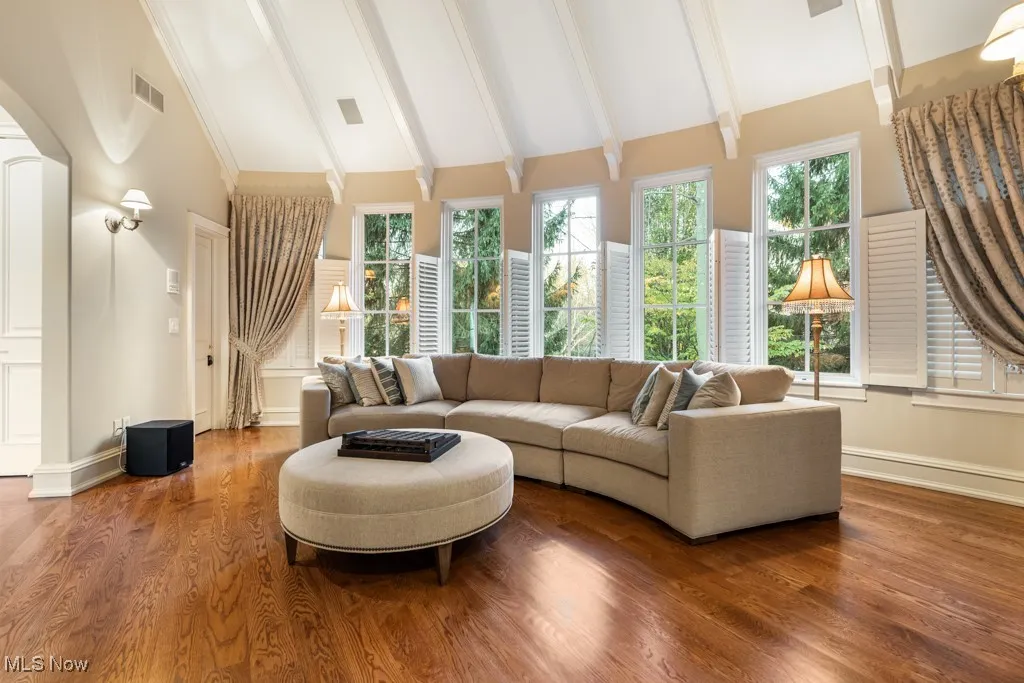 Living area with wood finished floors, baseboards, visible vents, high vaulted ceiling, and beam ceiling