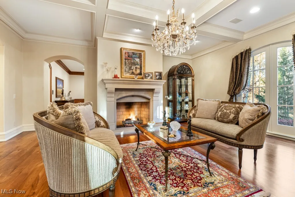 Living room featuring beam ceiling, wood finished floors, arched walkways, and a lit fireplace