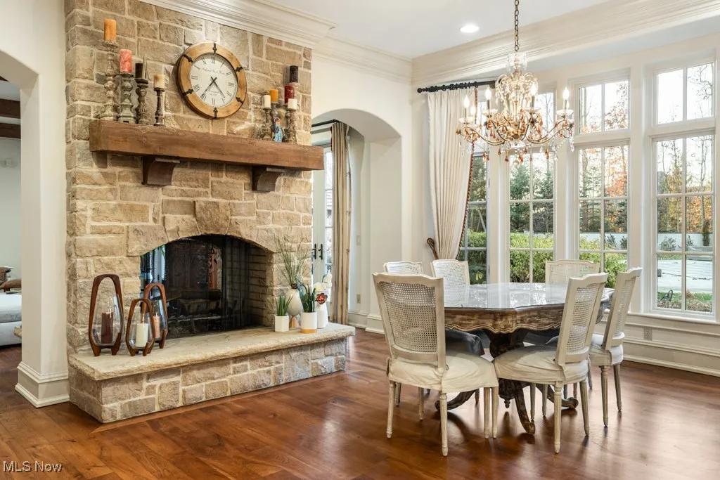 Dining area featuring a chandelier, ornamental molding, a stone fireplace, arched walkways, and dark wood-style flooring