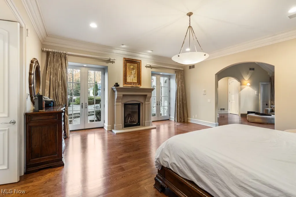 Bedroom with wood finished floors, arched walkways, french doors, crown molding, and access to outside