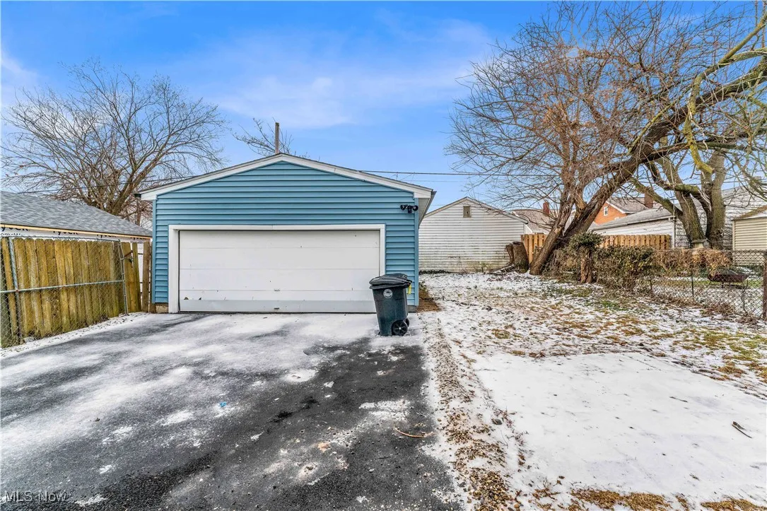 Snow covered garage with a detached garage and fence
