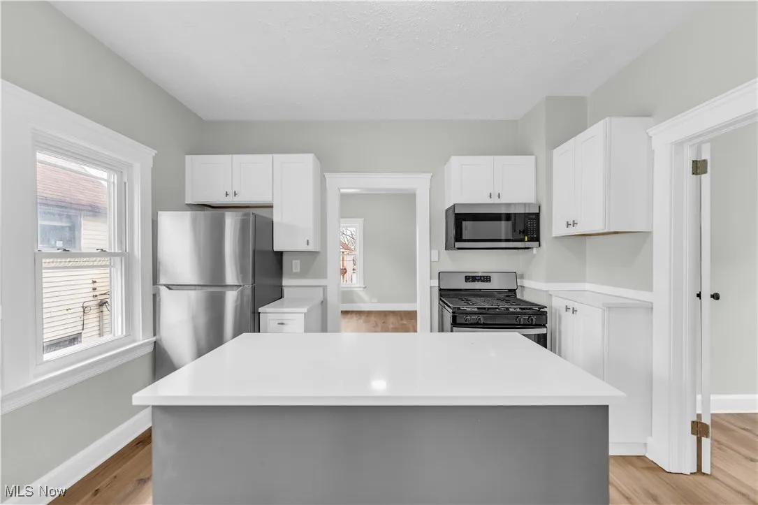 Kitchen featuring white cabinets, appliances with stainless steel finishes, light countertops, and light wood-style floors
