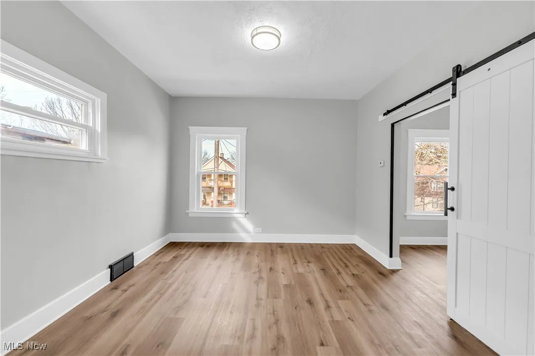 Spare room with visible vents, light wood-style flooring, baseboards, and a barn door