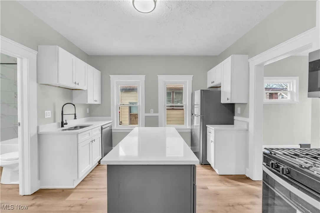 Kitchen featuring light wood finished floors, a center island, light countertops, appliances with stainless steel finishes, and a sink