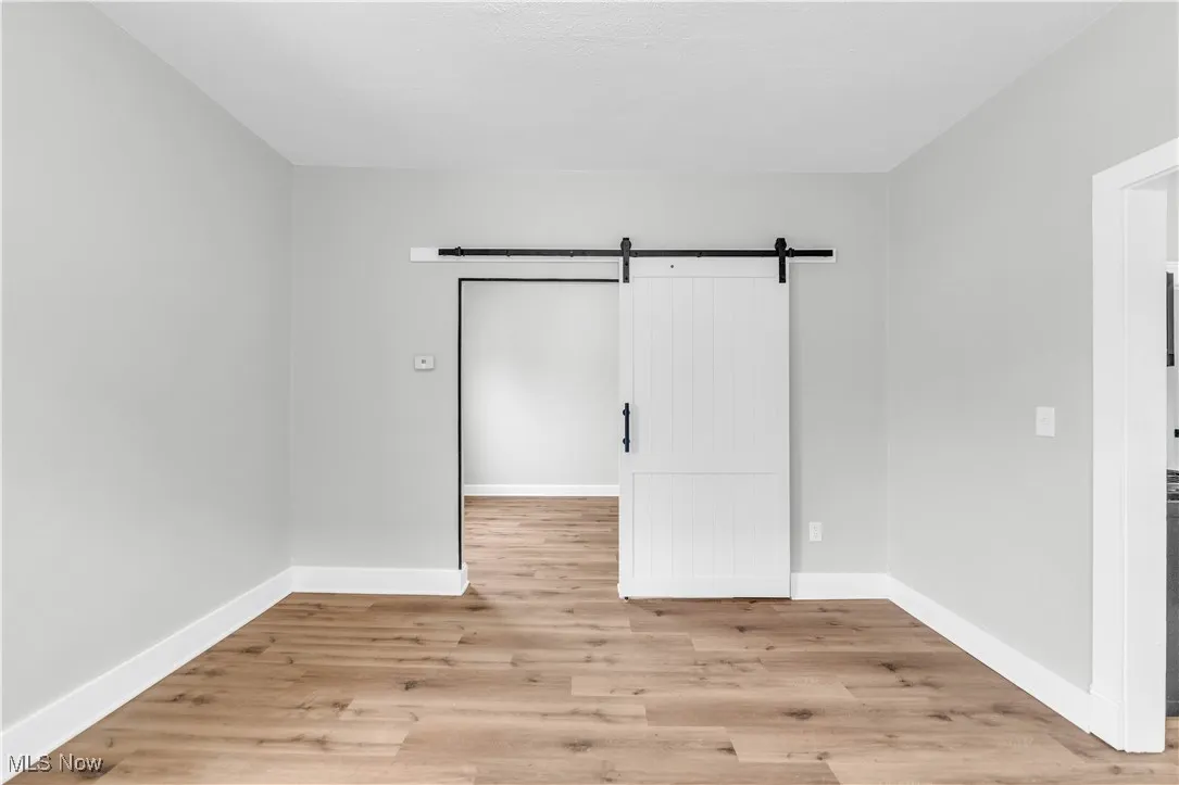 Empty room featuring a barn door, light wood-style floors, and baseboards