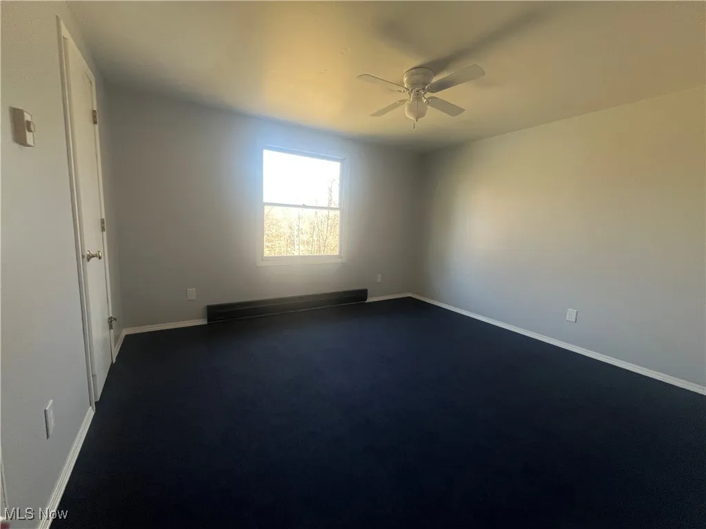 Unfurnished room with dark colored carpet, baseboards, baseboard heating, and ceiling fan