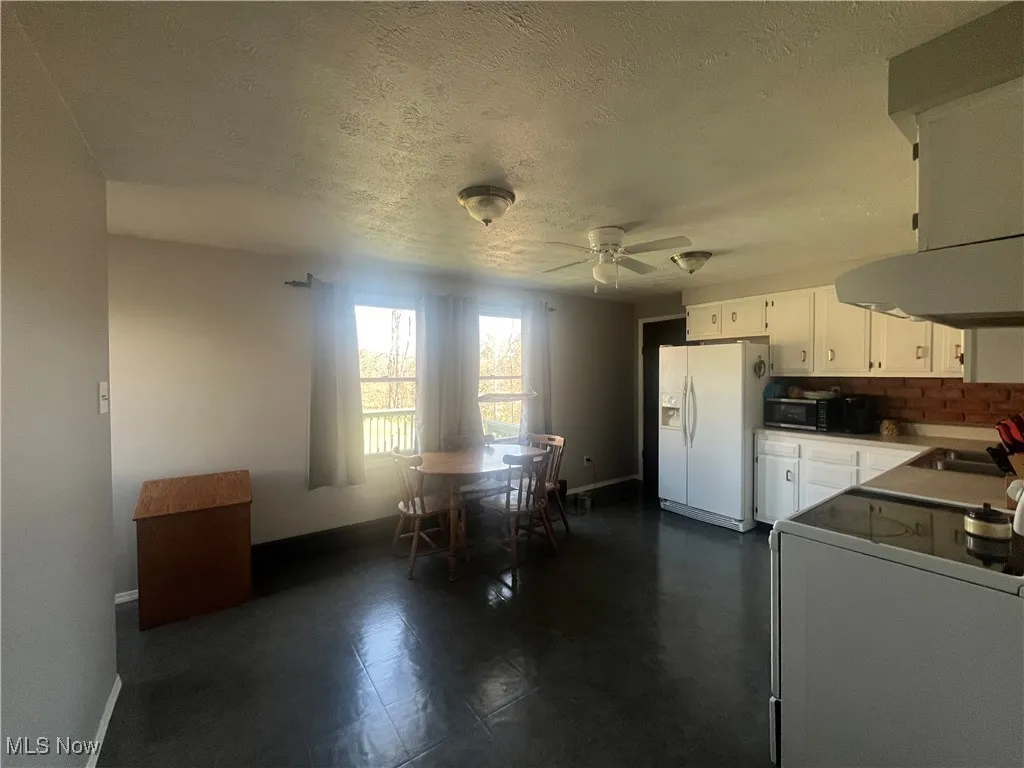 Kitchen with a sink, white cabinetry, white fridge with ice dispenser, stove, and ceiling fan
