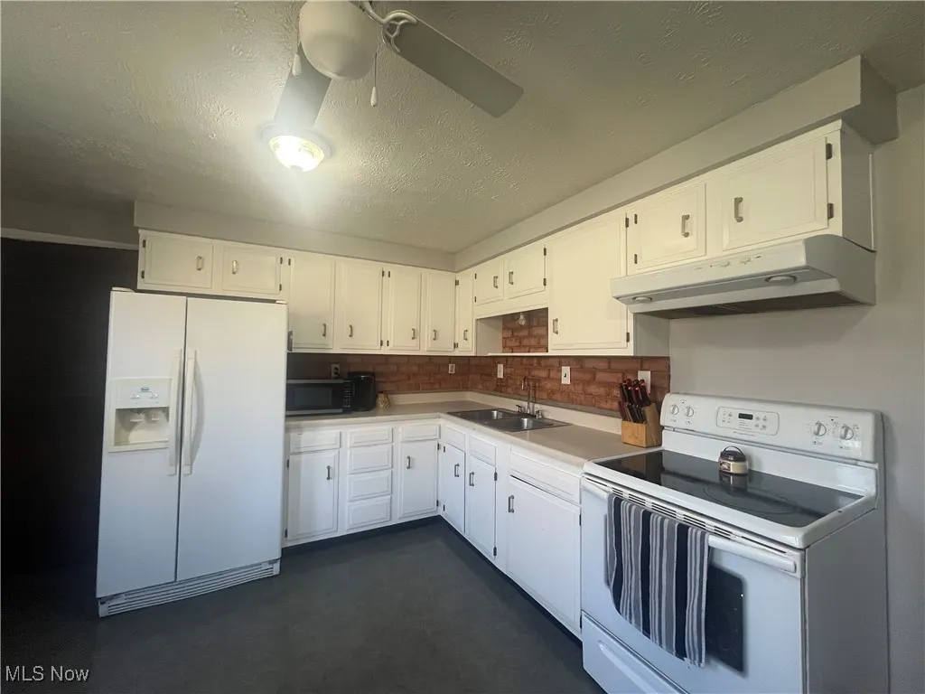 Kitchen featuring white cabinetry, white appliances, under cabinet range hood, and a sink