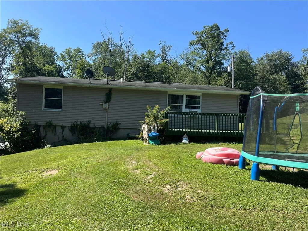 Back of property with a trampoline, a wooden deck, and a yard