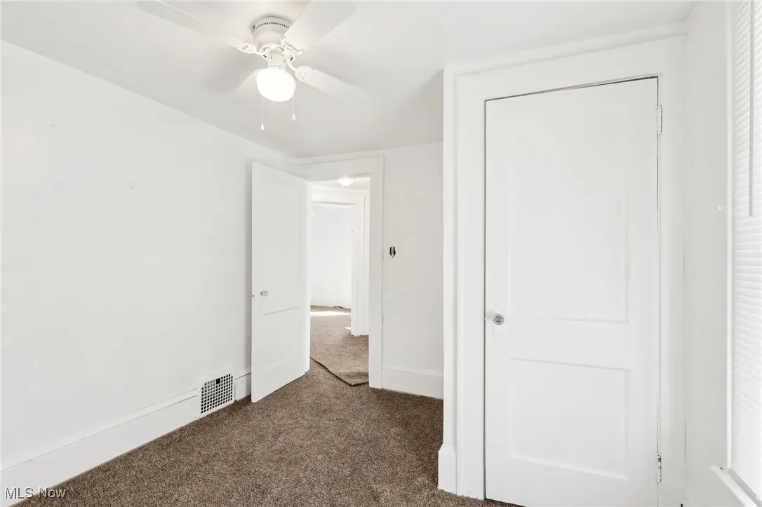Unfurnished bedroom with visible vents, baseboards, dark carpet, a closet, and a ceiling fan