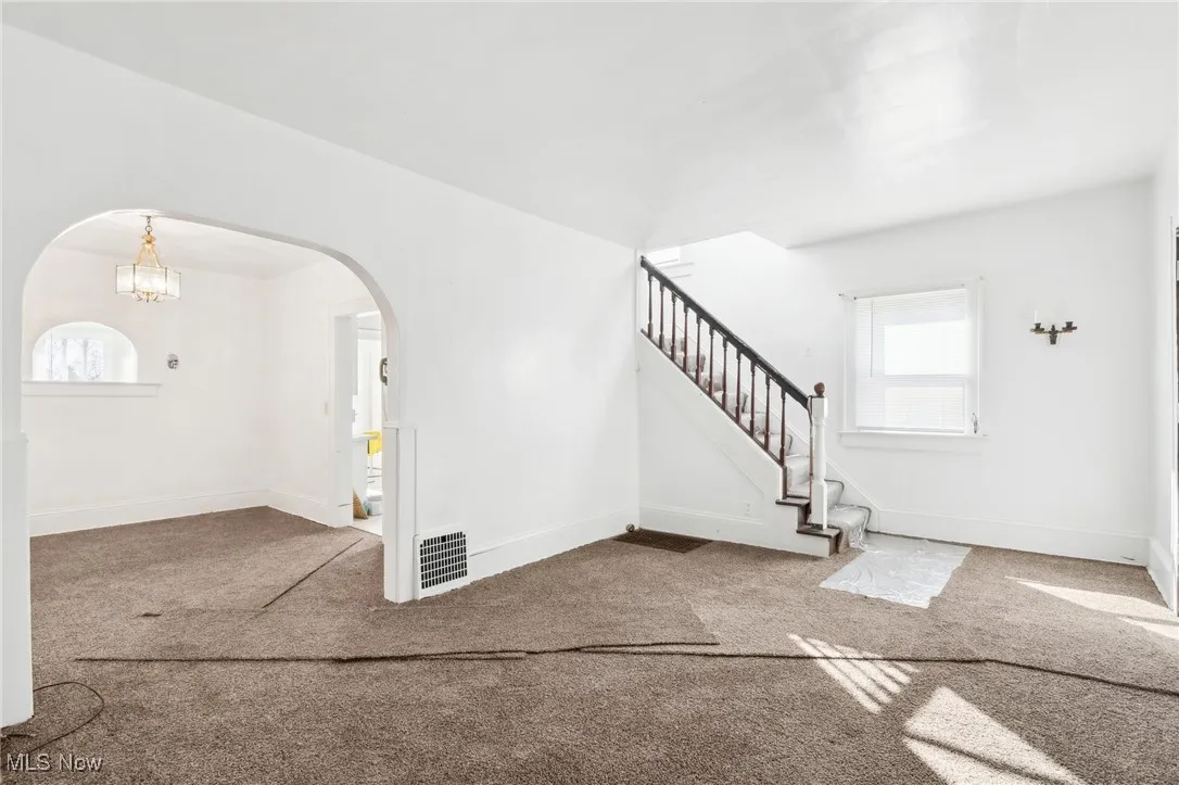 Carpeted entrance foyer with arched walkways, stairway, visible vents, and baseboards