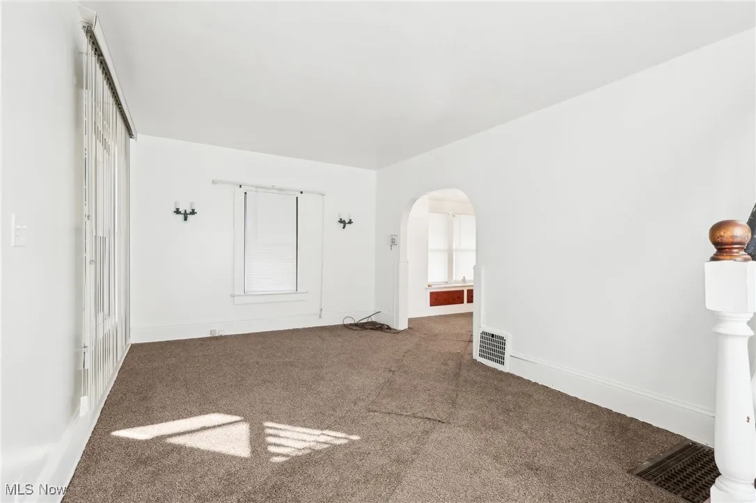 Carpeted empty room featuring arched walkways, visible vents, and baseboards