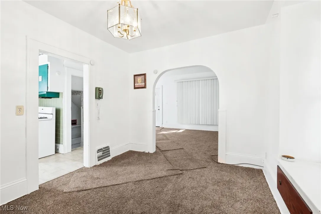 Carpeted spare room featuring visible vents, a notable chandelier, washer / clothes dryer, arched walkways, and baseboards