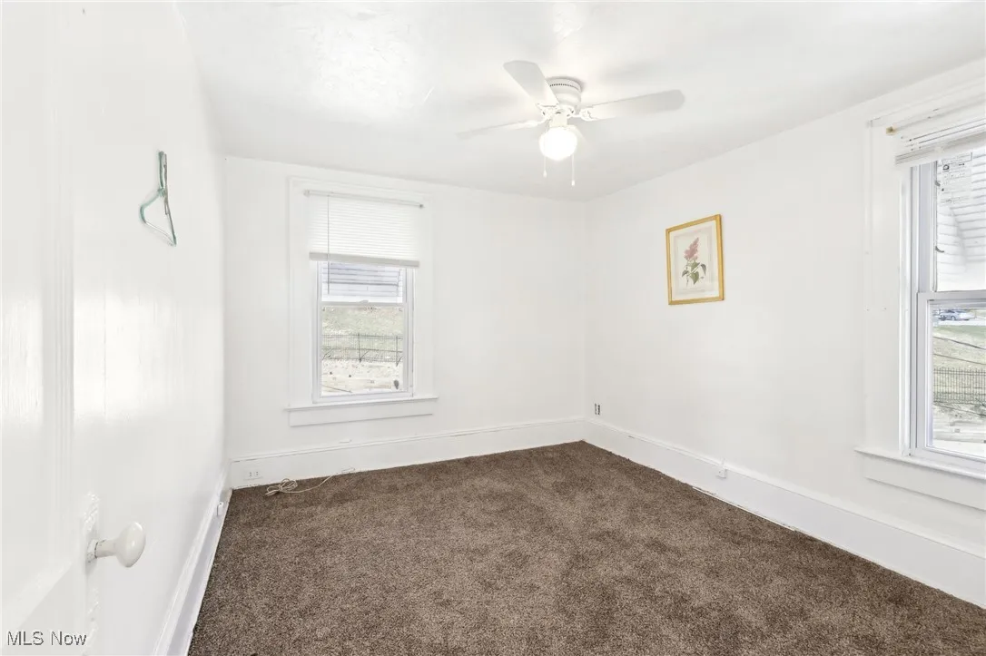 Empty room featuring baseboards, dark carpet, and ceiling fan