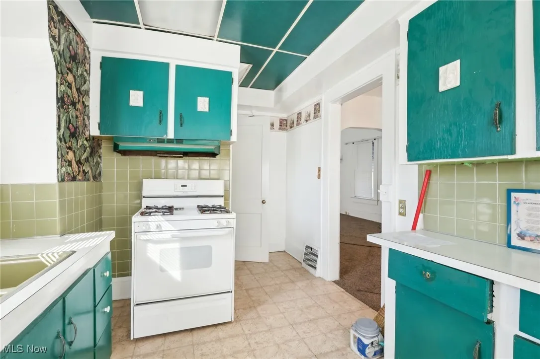 Kitchen with visible vents, decorative backsplash, light countertops, under cabinet range hood, and white gas range