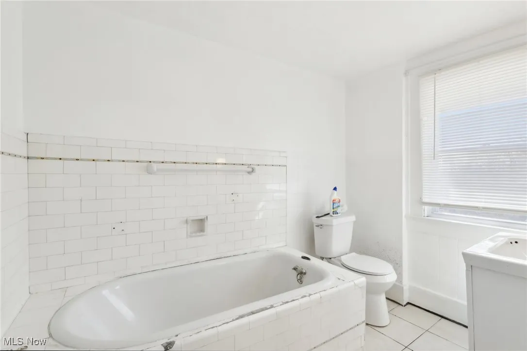 Bathroom featuring tiled bath, tile patterned flooring, and toilet