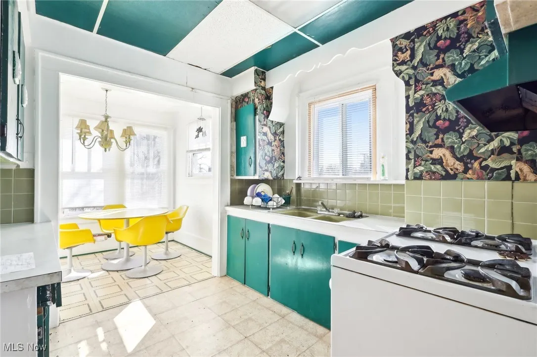 Kitchen with light floors, an inviting chandelier, a sink, extractor fan, and white gas range oven