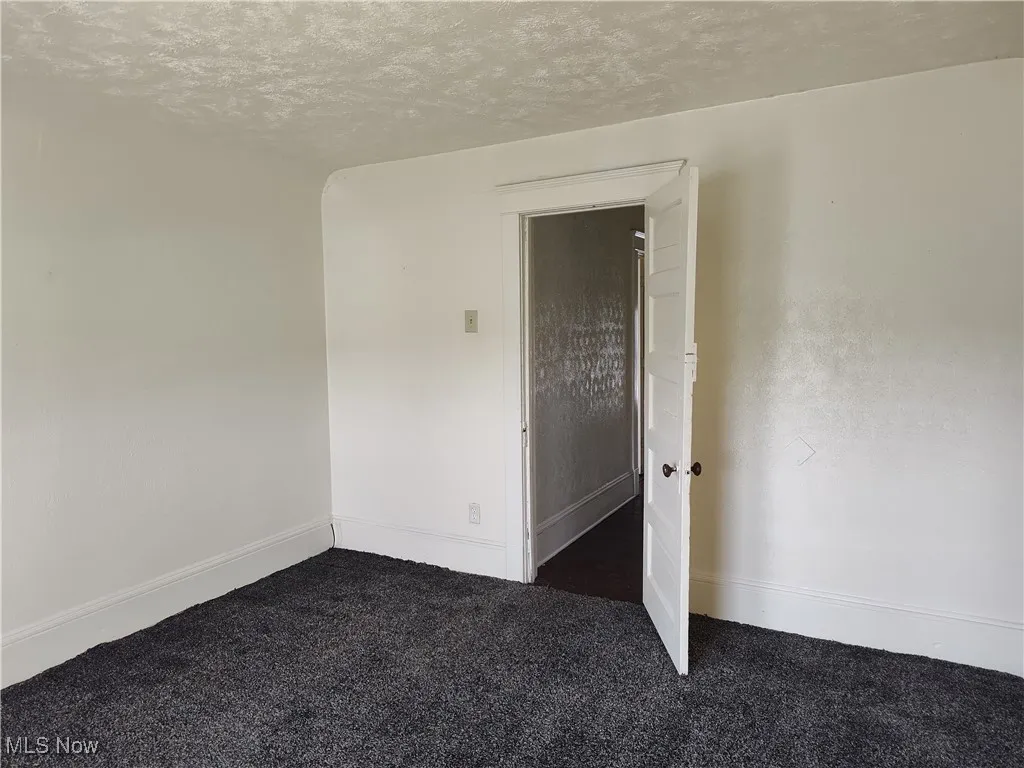 Empty room with dark carpet, a textured ceiling, and baseboards