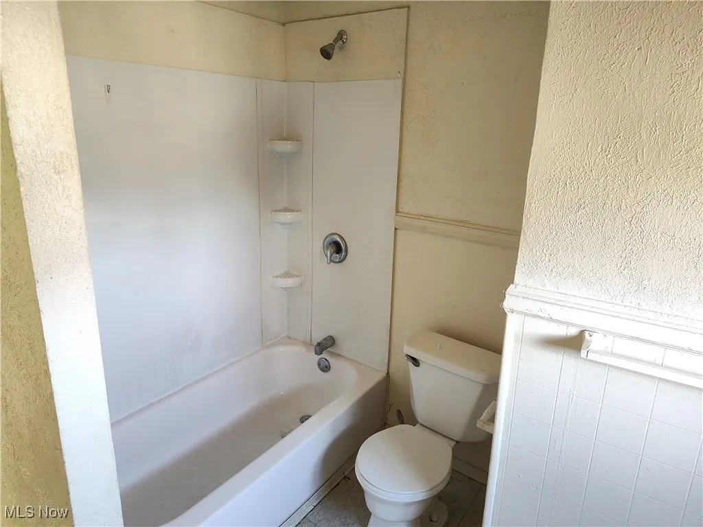 Full bathroom with tub / shower combination, toilet, and a textured wall