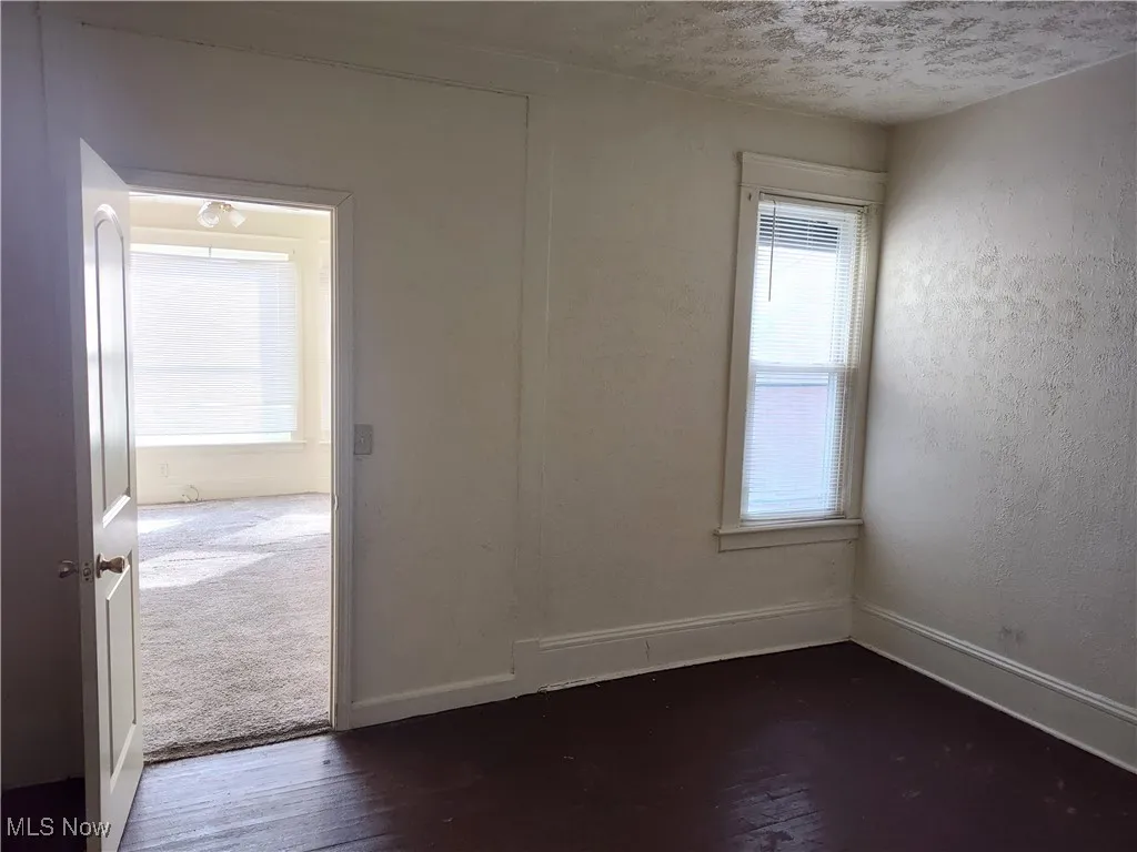 Spare room with dark wood-style floors, baseboards, a textured wall, and a textured ceiling