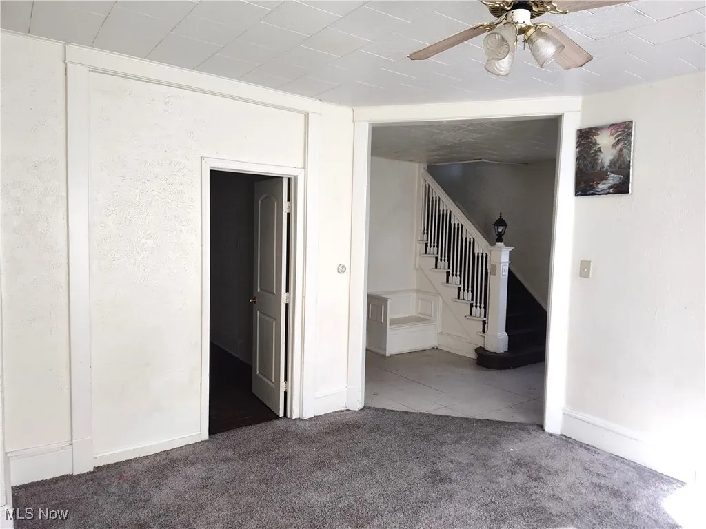 Carpeted empty room featuring stairway, baseboards, and ceiling fan