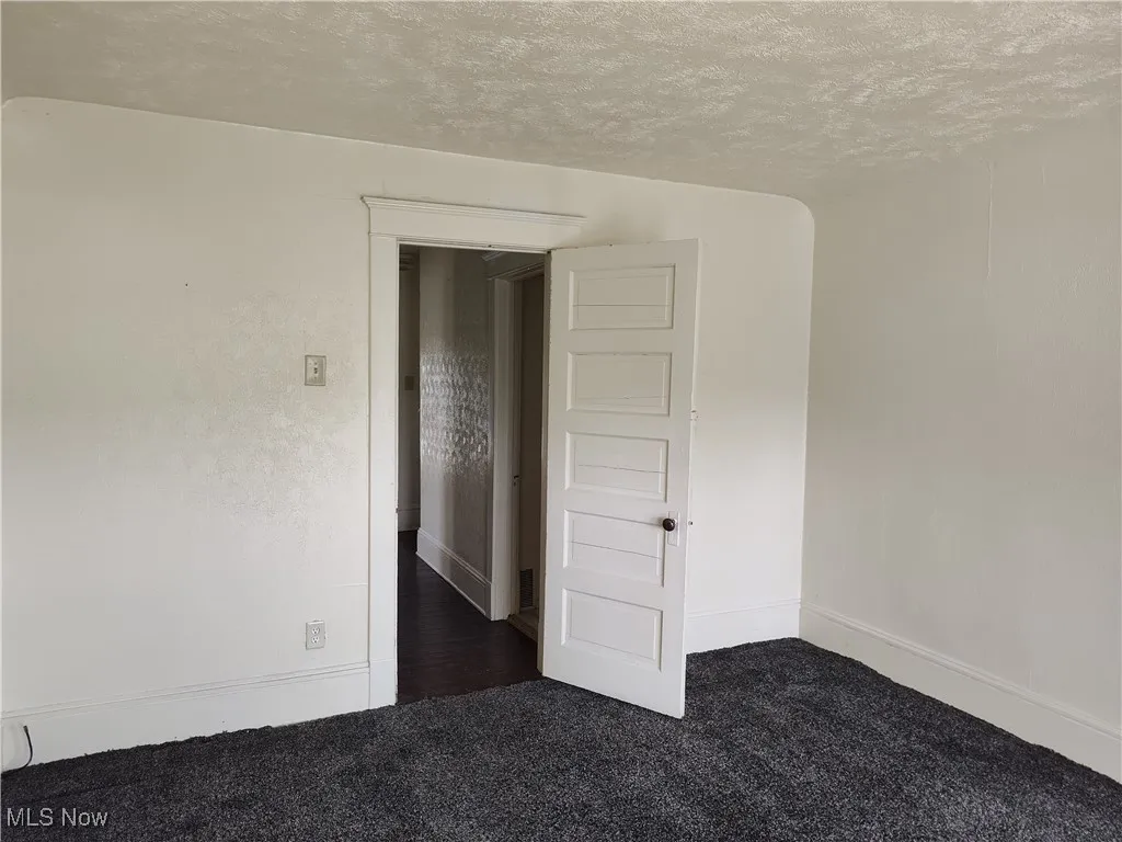 Unfurnished room featuring a textured ceiling, baseboards, and dark colored carpet