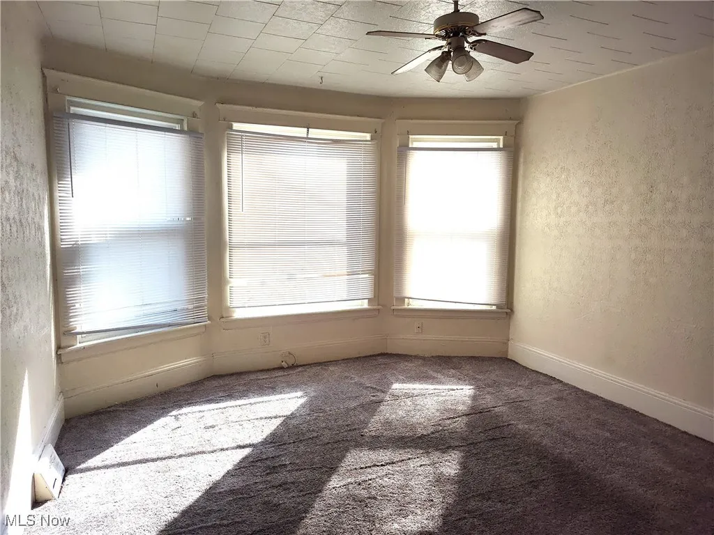 Carpeted spare room featuring baseboards, a ceiling fan, and a textured wall