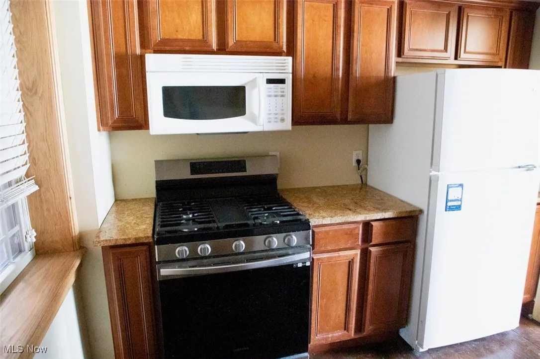 Kitchen with brown cabinetry, white appliances, and light stone counters