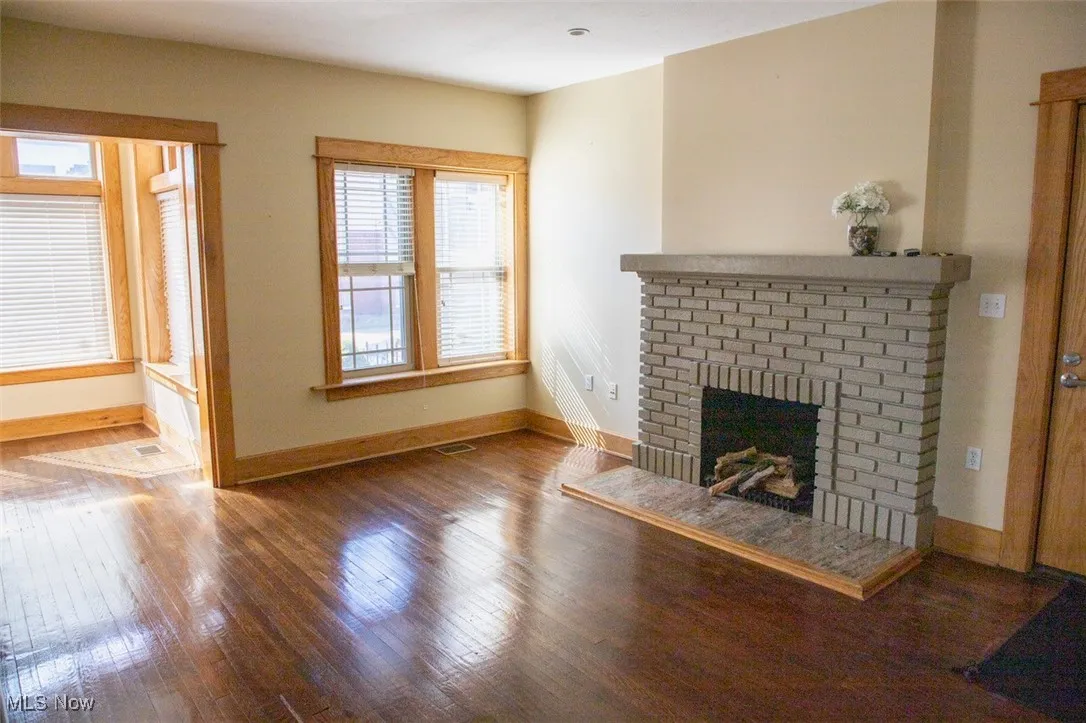 Unfurnished living room featuring hardwood / wood-style floors, a brick fireplace, visible vents, and baseboards