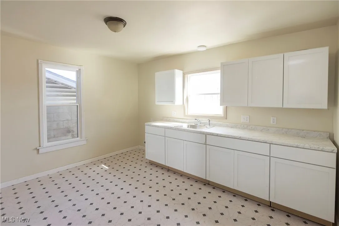 Kitchen featuring light floors, baseboards, a sink, light countertops, and white cabinetry
